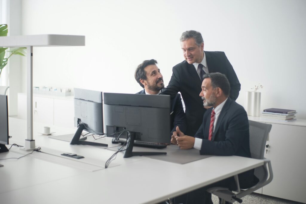 Eurocredit Mexico SAPI de CV SOFOM ENR Three business executives in suits collaborating around dual monitors in a modern office setting.